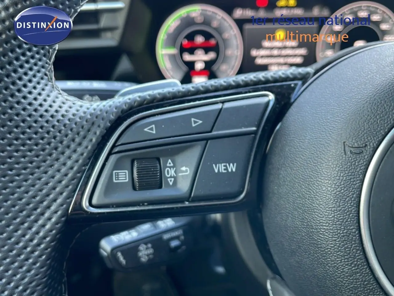 Gros plan sur les commandes multifonctions du volant perforé d'une Audi A3 Sportback blanc ibis, tableau de bord numérique en arrière-plan.