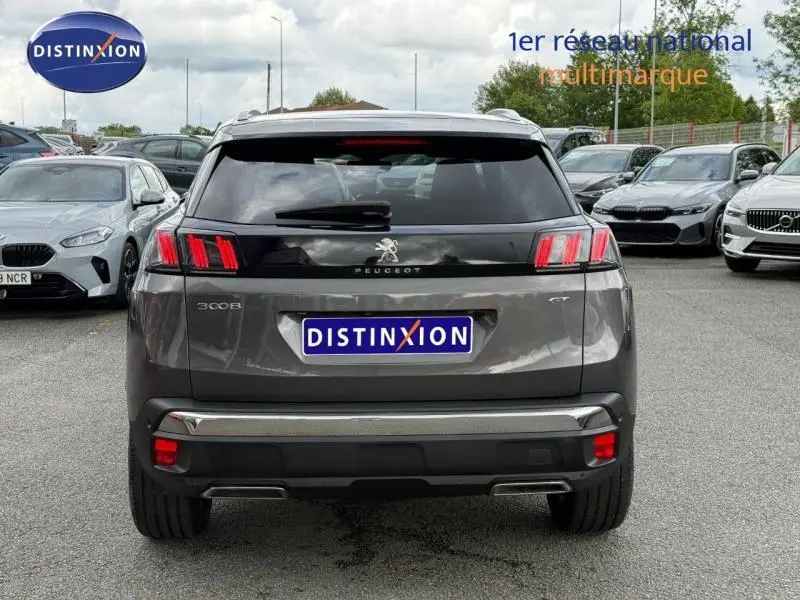 Vue arrière d'un Peugeot 3008 Gris Platinium 2024 avec feux arrière à trois griffes et logo central sur un parking.