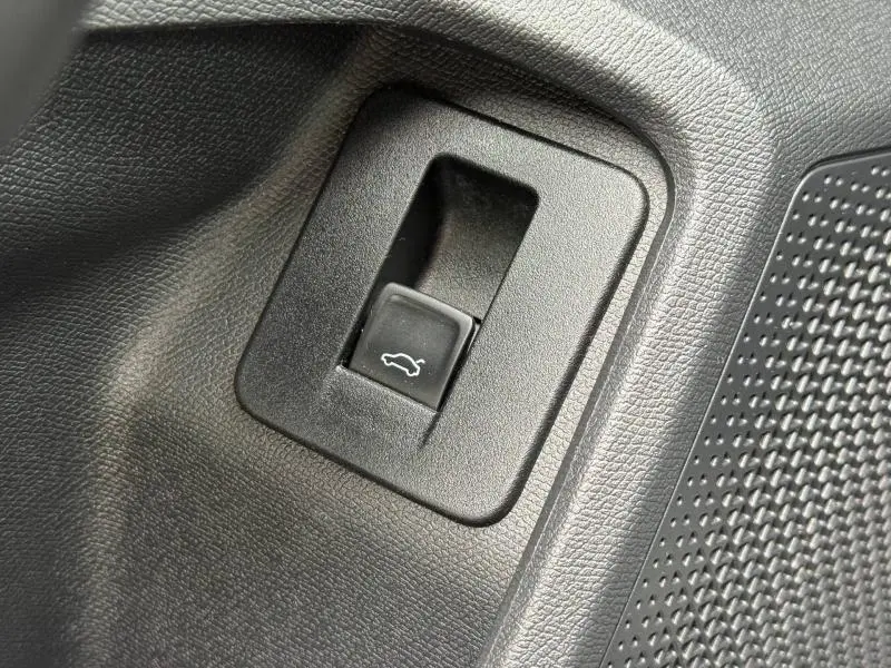 Gros plan sur le bouton d'ouverture du coffre intérieur du CUPRA Formentor 1.5 eTSI Hybrid 2025, entouré de plastique texturé noir.