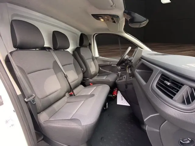 Vue intérieure côté conducteur du Renault Trafic Fourgon blanc 2025, montrant les sièges gris et le tableau de bord moderne.