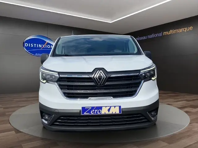 Vue frontale d'un Renault Trafic Fourgon blanc 2025 avec calandre noire et phares LED allumés en showroom.