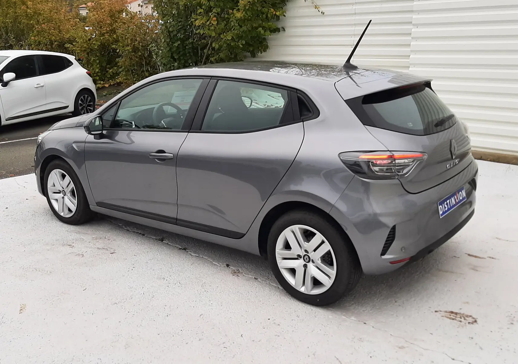 Renault Clio V gris schiste vue 3/4 arrière côté gauche, avec feux arrière allumés et jantes alliage.