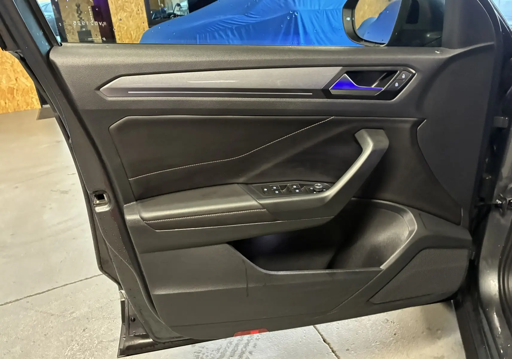 Vue intérieure de la porte avant gauche du Volkswagen T-Roc gris, avec commandes des vitres et poignée intégrée.