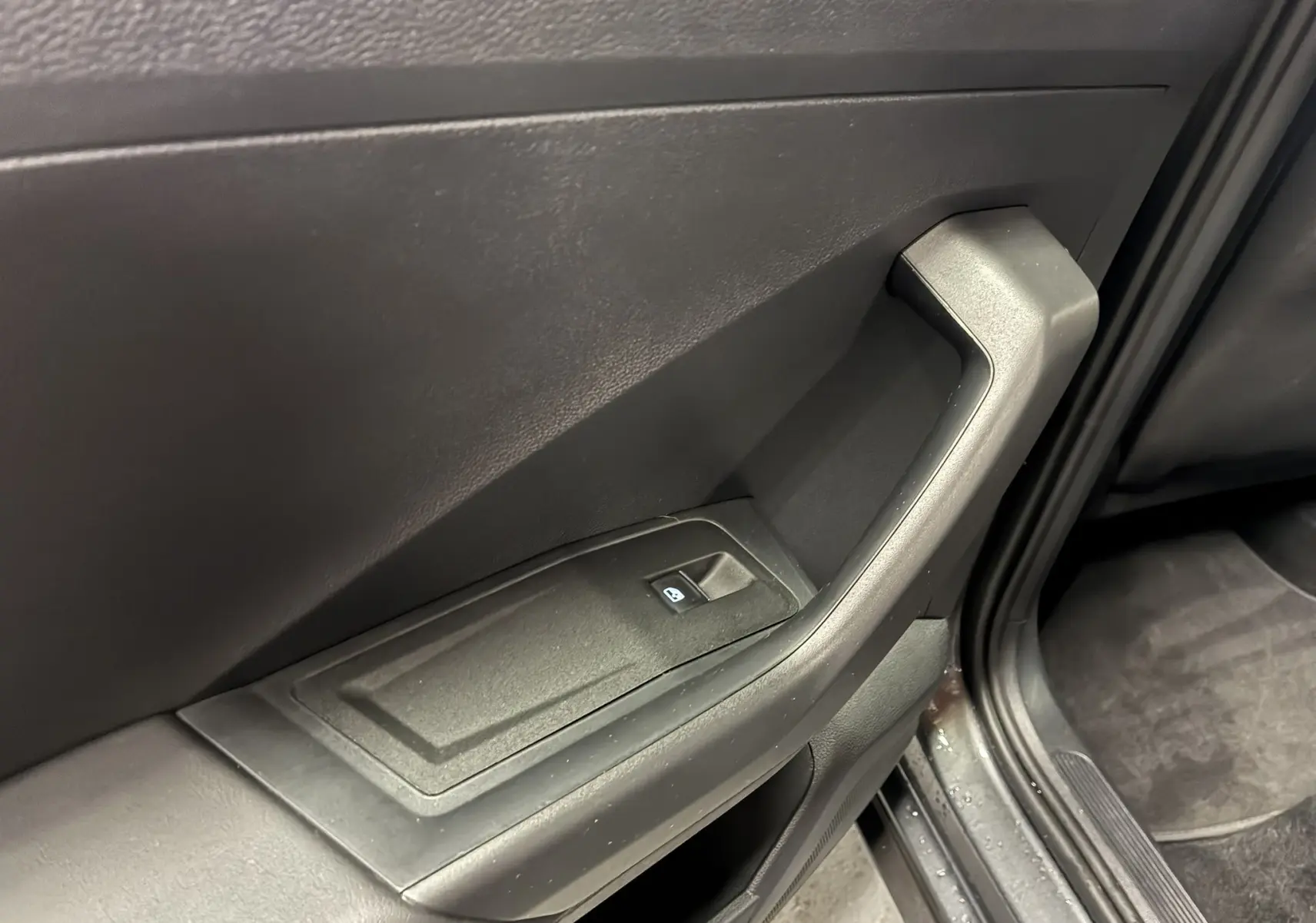 Gros plan sur la poignée intérieure et la commande de vitre côté gauche d’un Volkswagen T-Roc gris 2023.