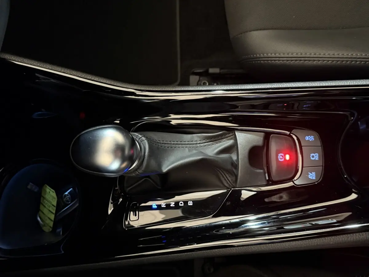 Vue rapprochée du levier de vitesses automatique noir brillant du Toyota C-HR 1.8 Hybride gris foncé, avec bouton frein à main électronique allumé.