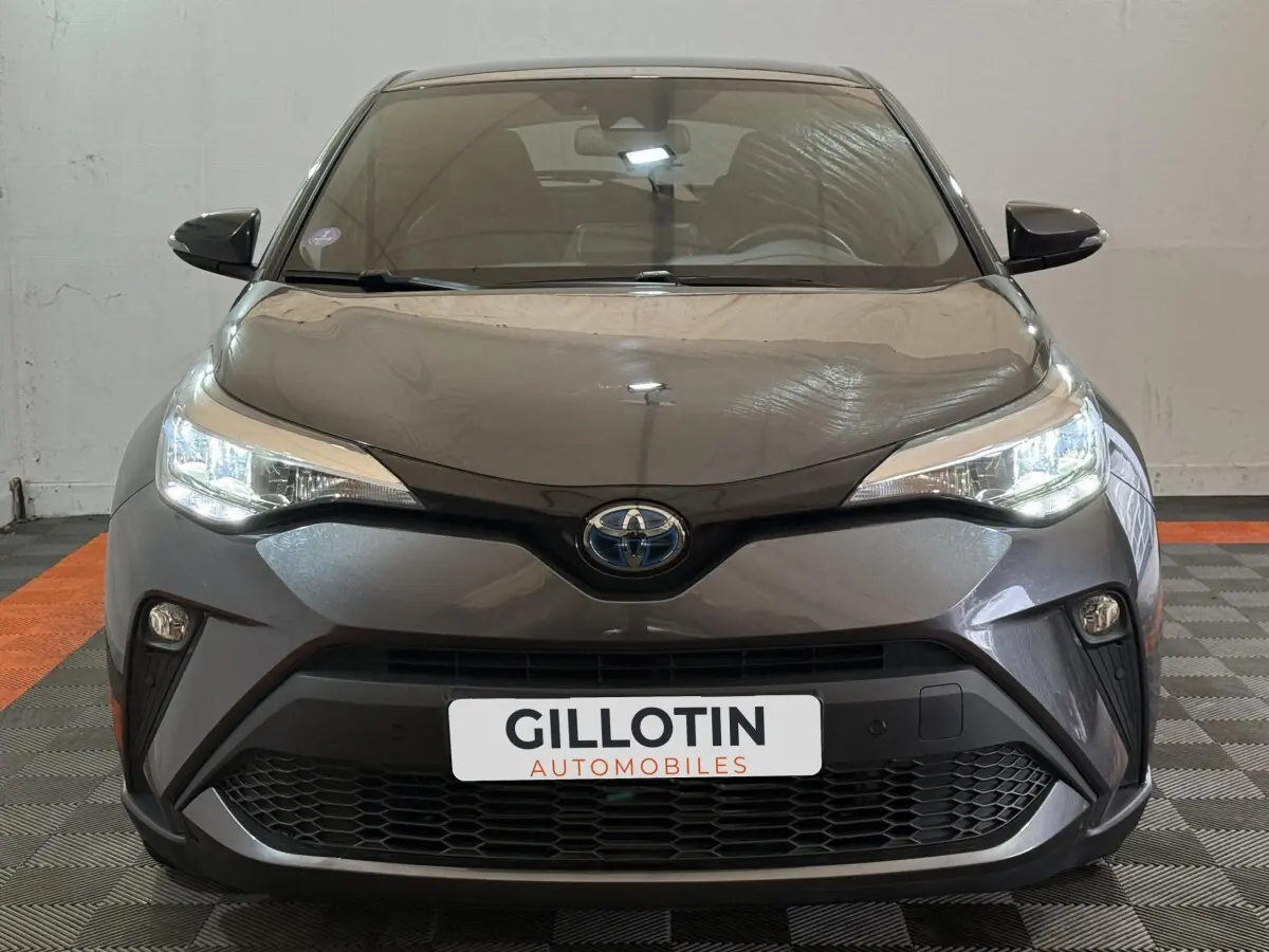 Vue frontale d'une Toyota C-HR 1.8 Hybride 122 Edition gris foncé avec phares LED allumés et calandre noire.