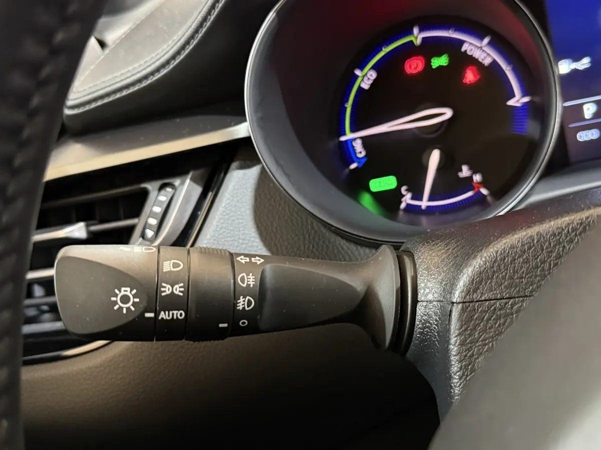 Gros plan sur la commande des phares à gauche du volant dans l’habitacle du Toyota C-HR gris foncé.