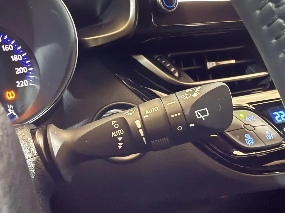 Gros plan sur la commande d’essuie-glace à gauche du volant du Toyota C-HR gris foncé, avec tableau de bord partiellement visible.