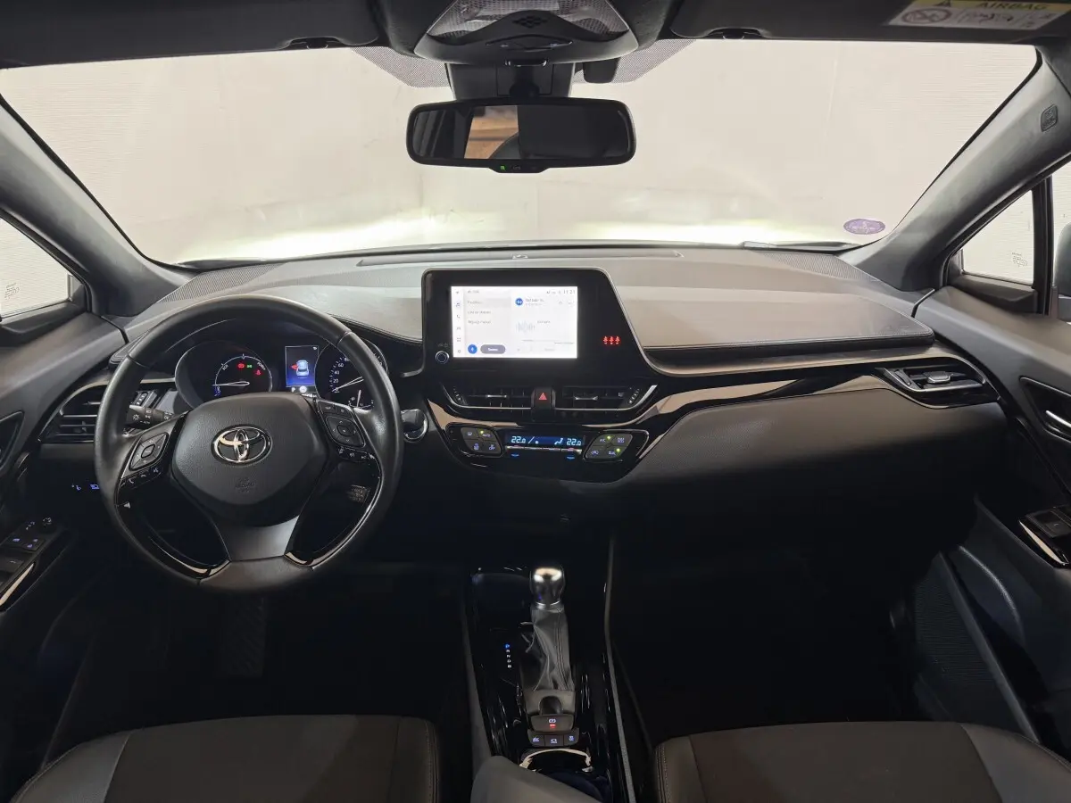 Vue intérieure frontale du tableau de bord noir du Toyota C-HR 1.8 Hybride 2022 avec écran tactile central et volant multifonctions.