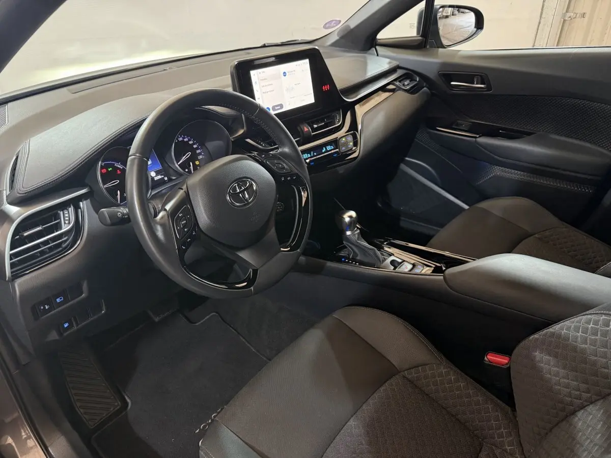 Vue intérieure côté conducteur du Toyota C-HR 1.8 Hybride 2022 avec tableau de bord numérique et écran tactile central.