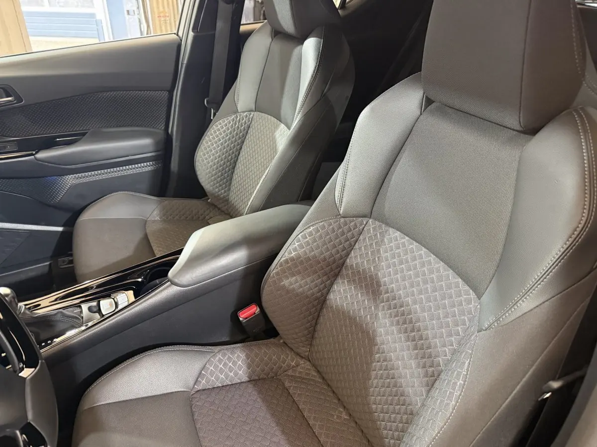 Vue intérieure rapprochée des sièges avant gris foncé avec console centrale brillante du Toyota C-HR 2022 hybride.