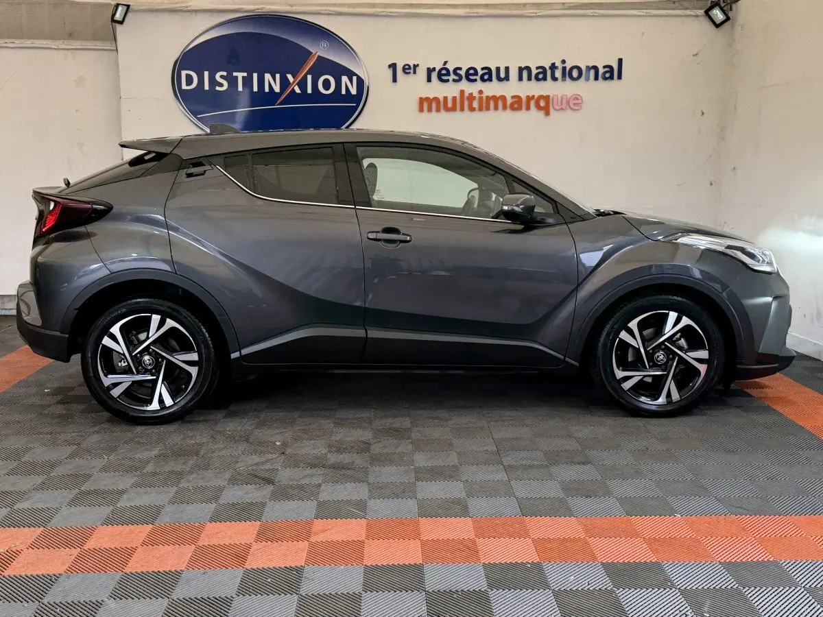 Toyota C-HR 1.8 Hybride gris foncé vu de profil côté gauche, avec jantes alliage et toit noir contrasté.