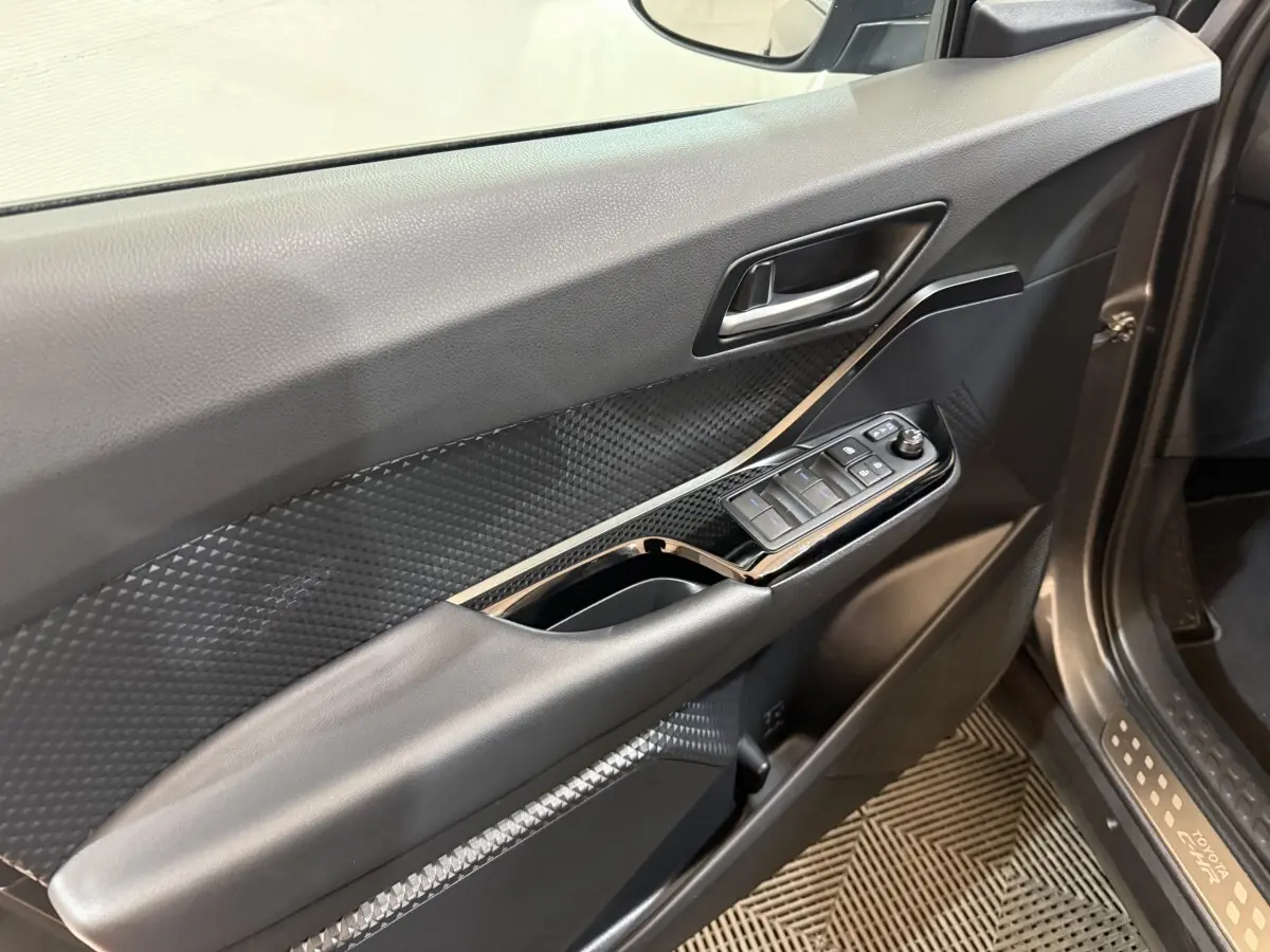 Vue intérieure du panneau de porte avant gauche du Toyota C-HR gris foncé, avec commandes électriques des vitres et poignée intégrée.