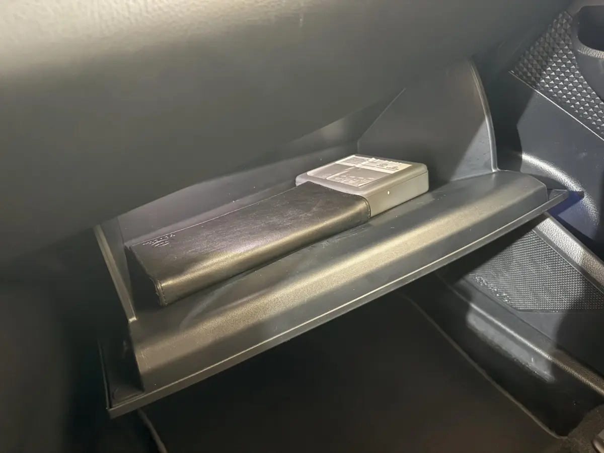 Gant de boîte à gants ouvert dans un Toyota C-HR 1.8 Hybride gris foncé, montrant un carnet et un boîtier électronique.