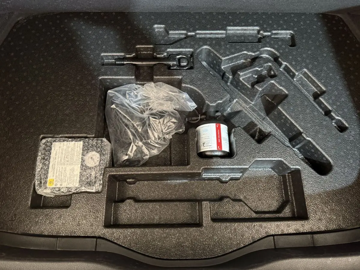 Vue plongeante sur le rangement noir dans le coffre du Toyota C-HR gris foncé, avec outils et kit de réparation pneus.