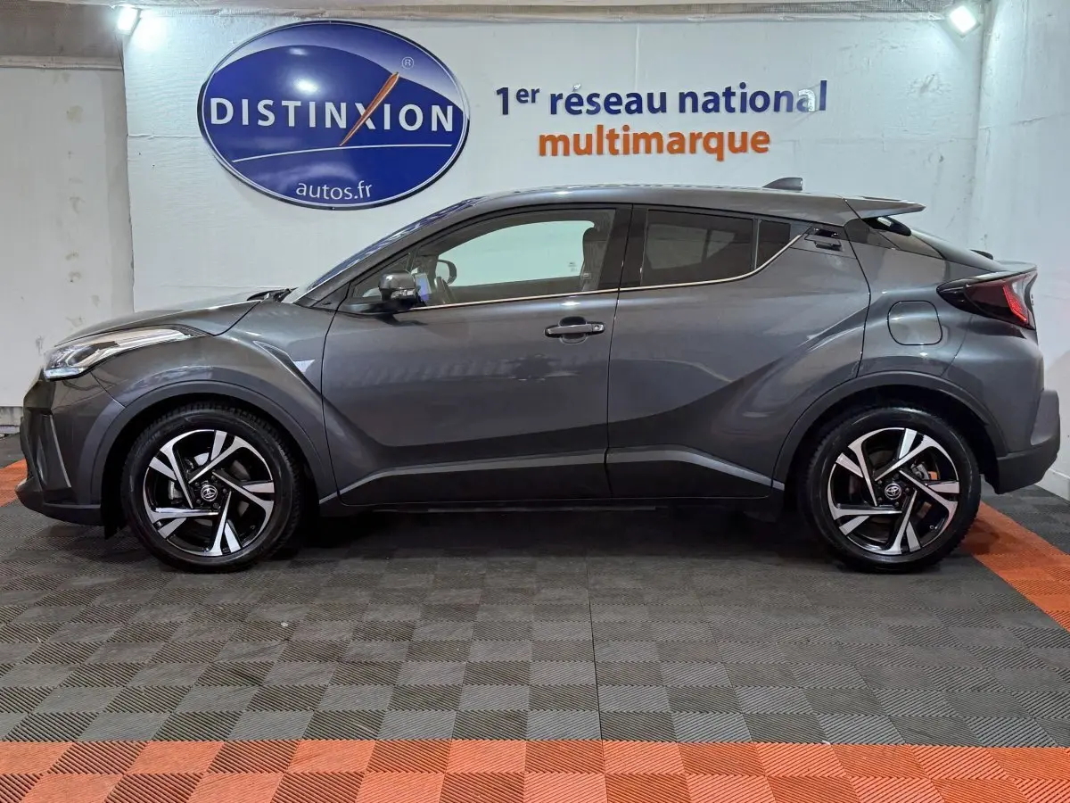 Profil latéral droit d'un Toyota C-HR 1.8 Hybride gris foncé avec jantes alliage et toit noir en intérieur showroom.