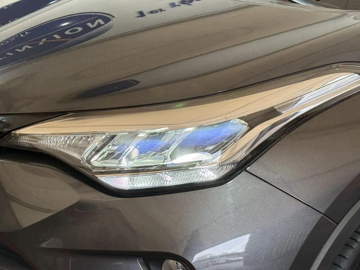 Gros plan sur le phare avant droit du Toyota C-HR 1.8 Hybride 2022 gris foncé avec carrosserie lisse et brillante.