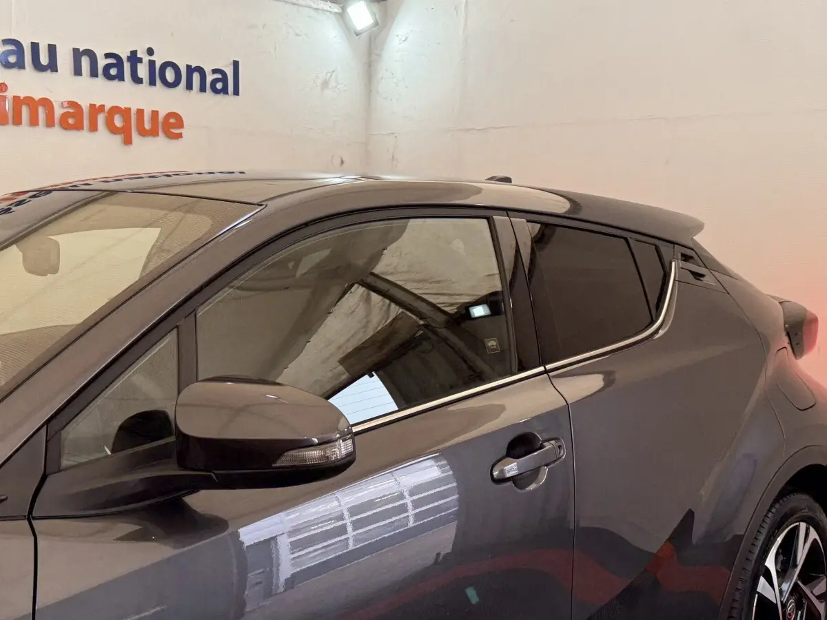 Vue côté gauche du Toyota C-HR 1.8 Hybride gris foncé, mettant en valeur la ligne de toit et les rétroviseurs intégrant clignotants.
