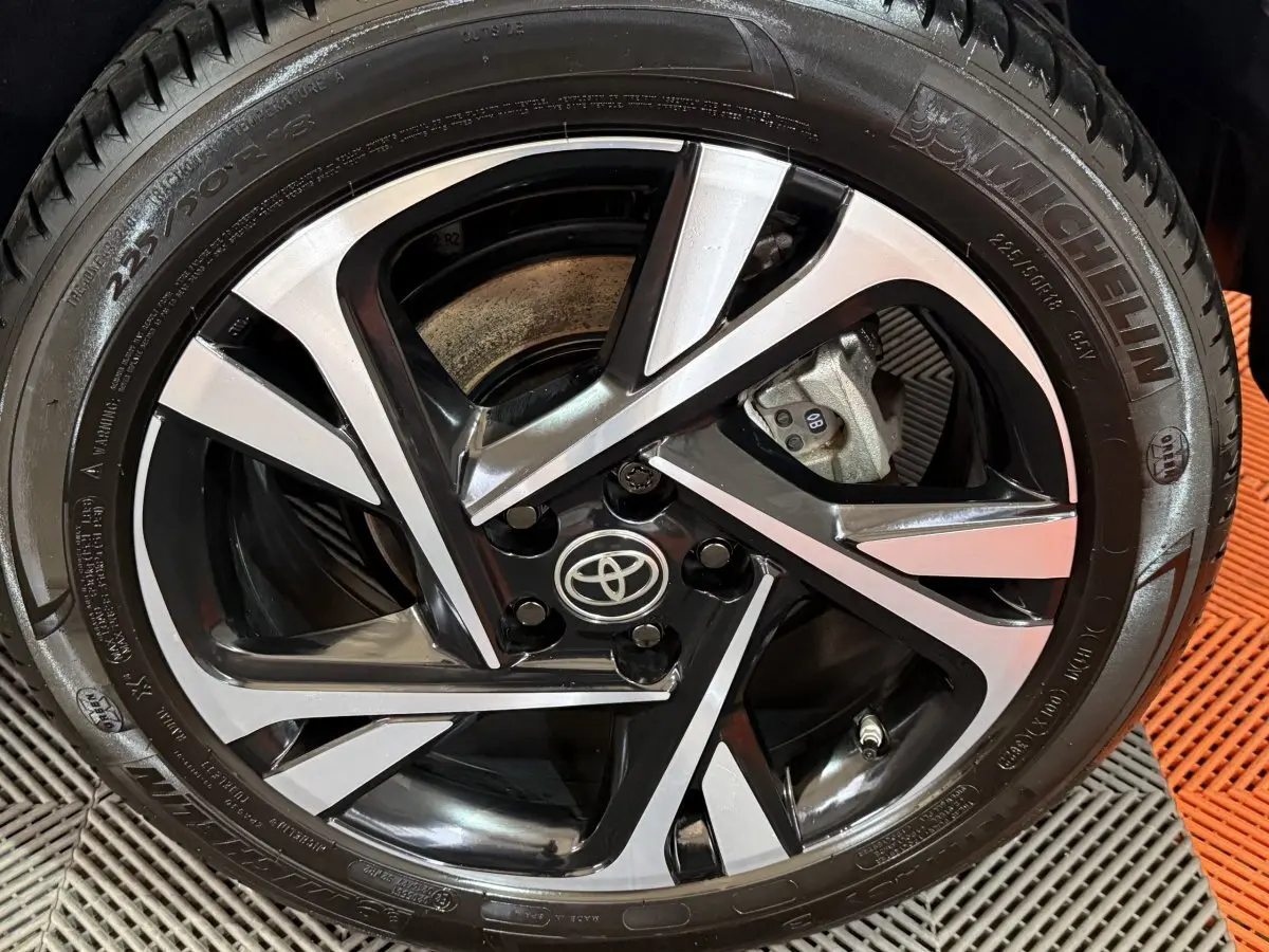 Gros plan sur la jante alliage bicolore noire et argentée avec logo Toyota au centre, pneu Michelin visible.