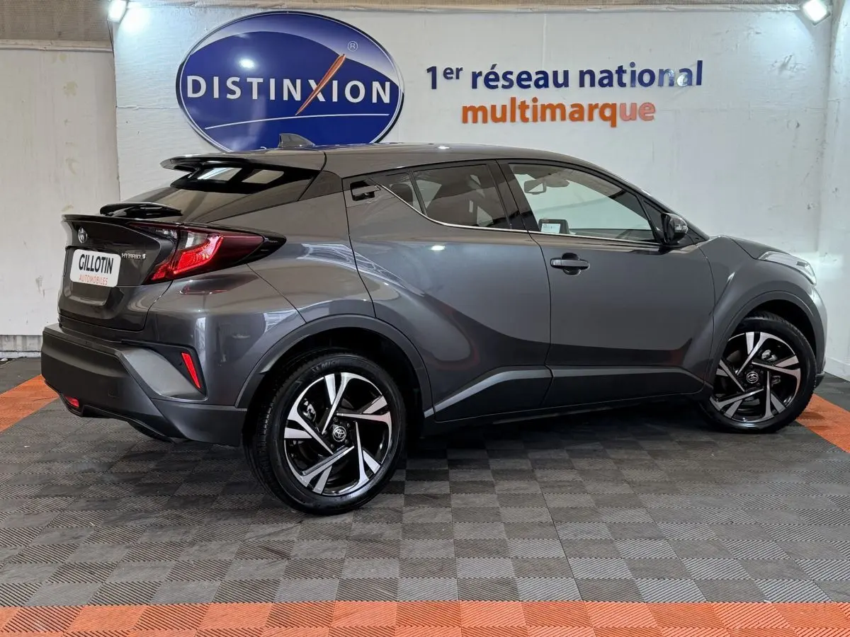 Vue latérale droite d’un Toyota C-HR 1.8 Hybride gris foncé avec jantes alliage et toit noir en arrière-plan showroom.