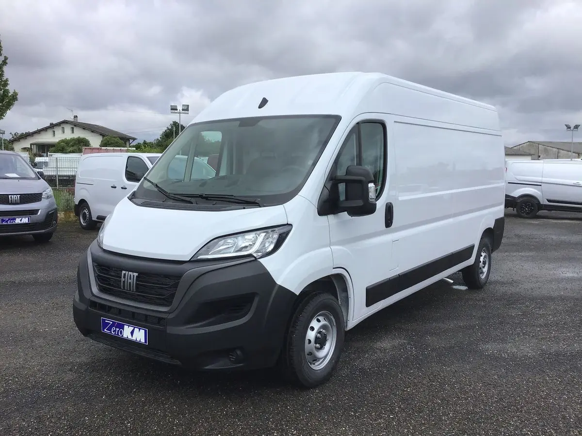 Fiat Ducato Fourgon blanc vu en 3/4 avant droit sur parking, avec calandre noire et rétroviseurs noirs.