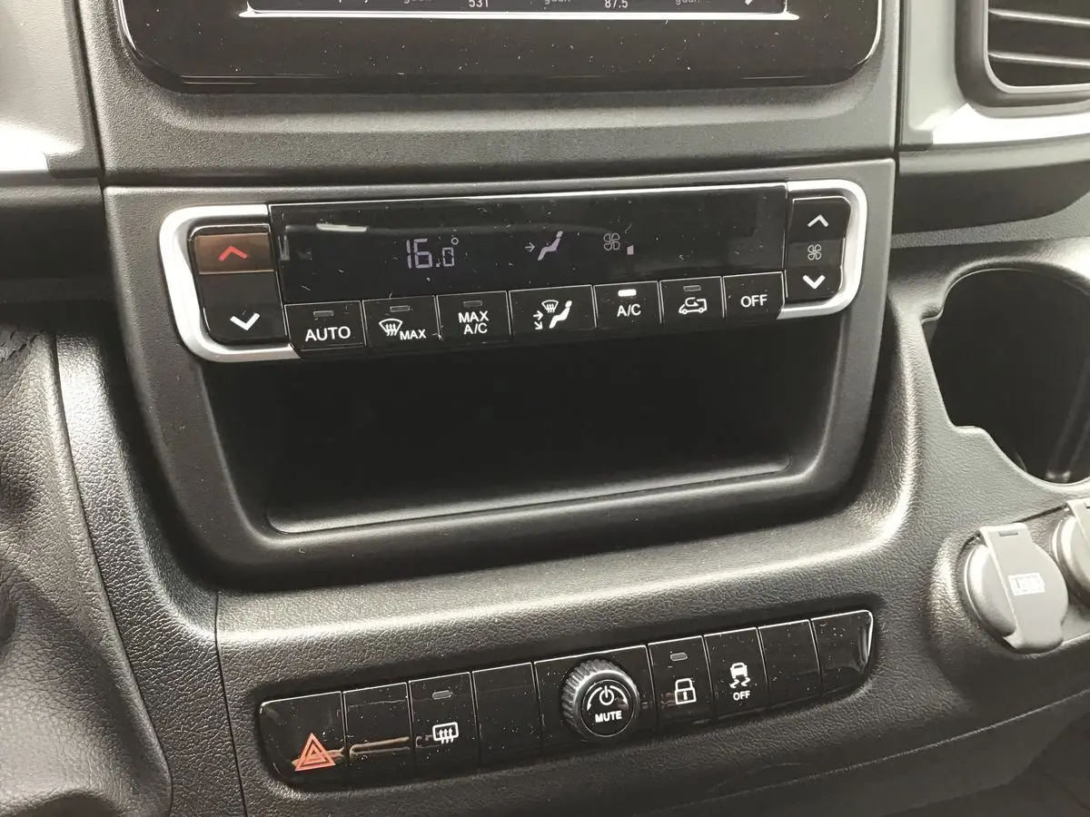 Gros plan sur la console centrale du Fiat Ducato Fourgon blanc 2023, mettant en valeur les commandes de climatisation et les boutons multifonctions.