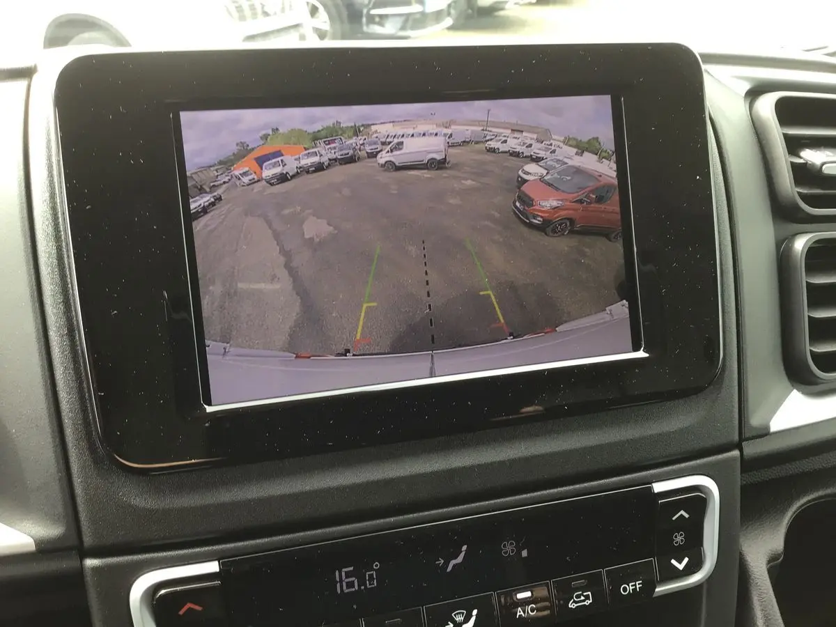 Écran tactile 7'' affichant la caméra de recul du FIAT Ducato blanc, vue arrière sur un parking avec plusieurs véhicules.