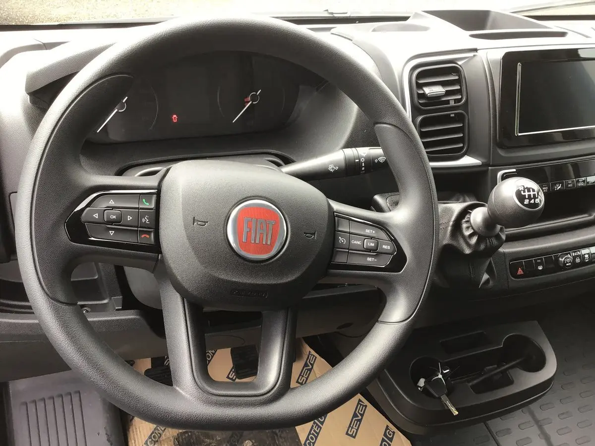 Vue intérieure du volant et tableau de bord noir du Fiat Ducato Fourgon 2023 avec levier de vitesse manuel et écran tactile.