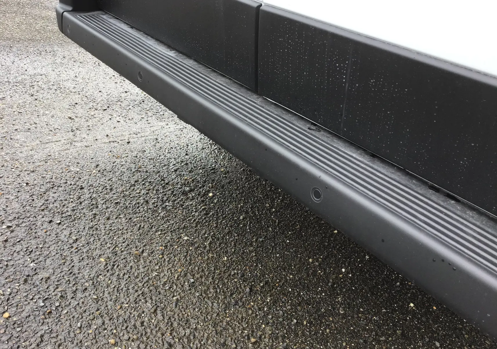 Gros plan sur la marche latérale noire du Fiat Ducato Fourgon blanc, côté droit, avec traces d'eau sur la carrosserie.