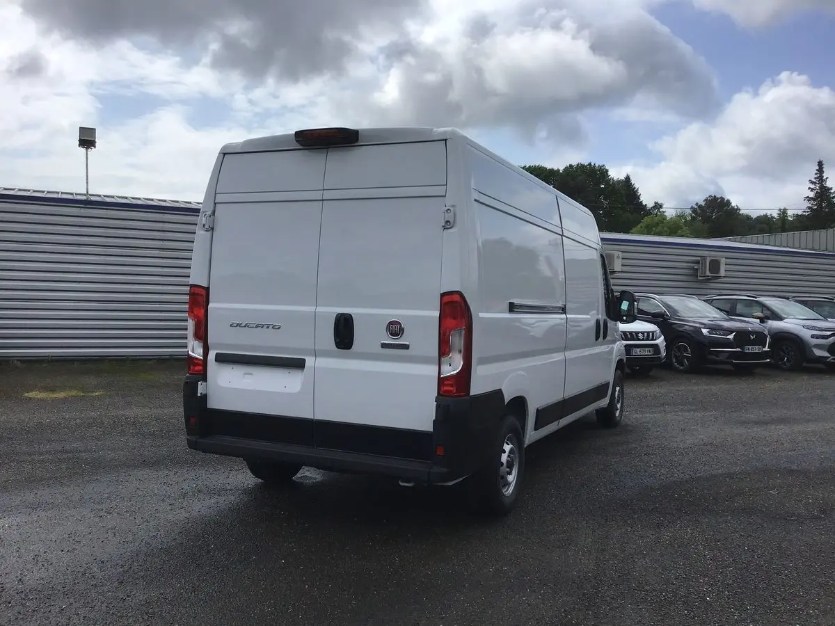 Vue 3/4 arrière d'un utilitaire FIAT Ducato blanc stationné, avec portes arrière fermées et feux rouges visibles.