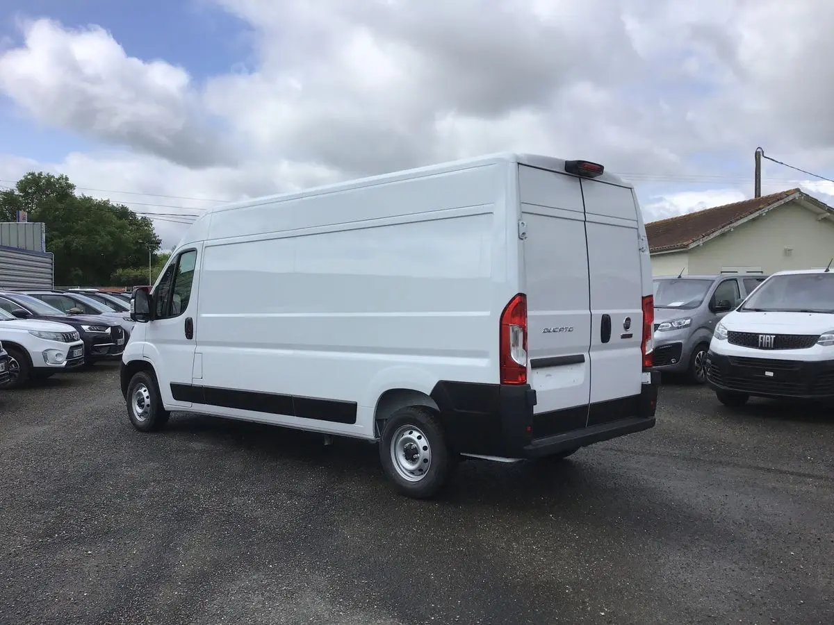 Fiat Ducato Fourgon blanc vu en 3/4 arrière droit sur un parking, avec portes arrière fermées et jantes acier.