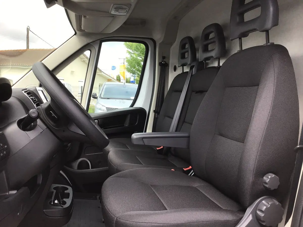 Vue intérieure côté conducteur du FIAT Ducato Fourgon blanc 2023, montrant les sièges noirs et le tableau de bord technologique.