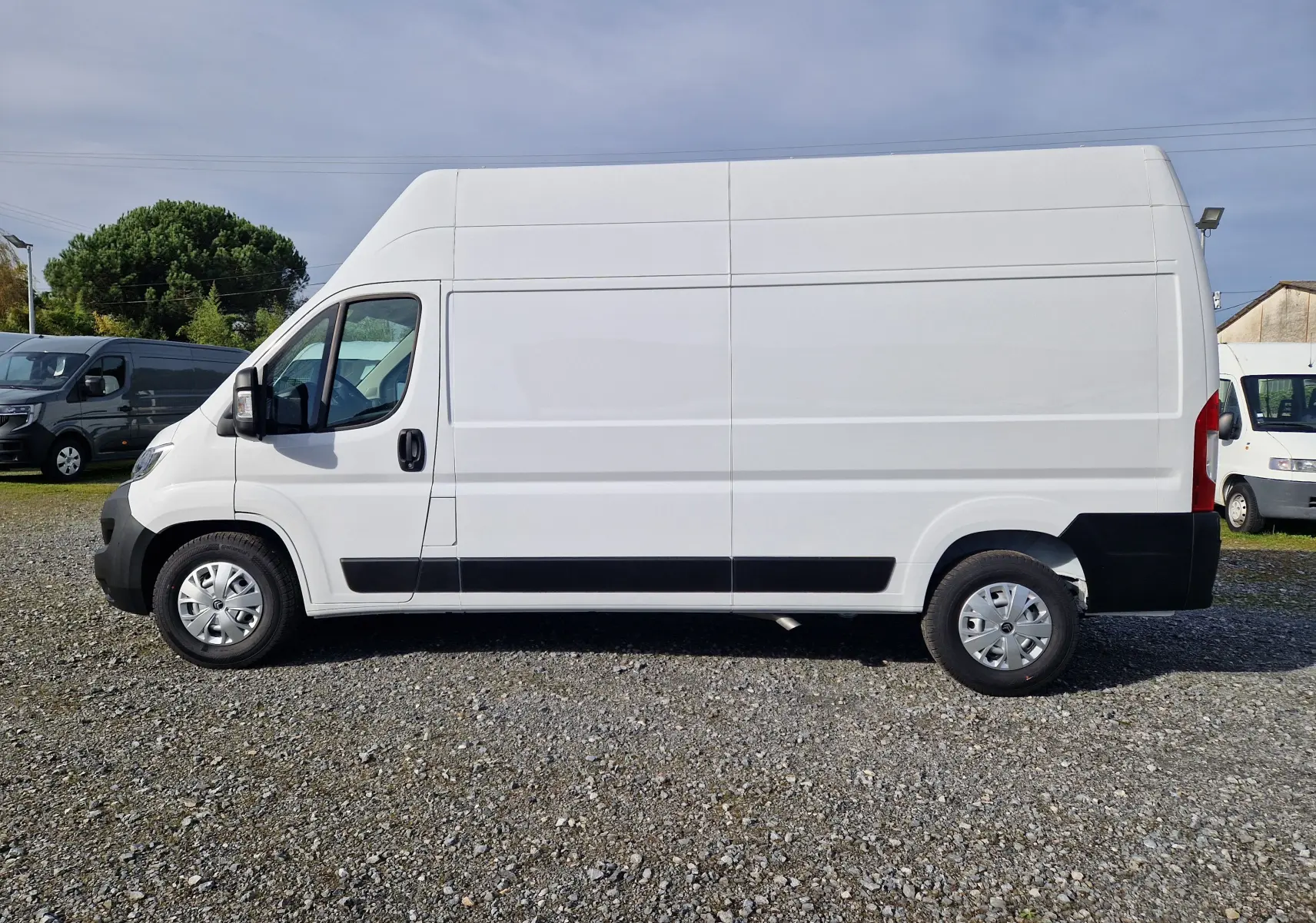 Vue de profil côté gauche d'un utilitaire blanc Citroën Jumper L3H3 2023 avec toit surélevé sur un sol gravillonné.