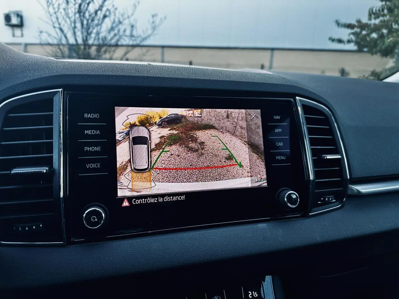 Écran tactile du tableau de bord d’un Skoda Karoq blanc 2024 montrant la caméra de recul avec guidage au stationnement.