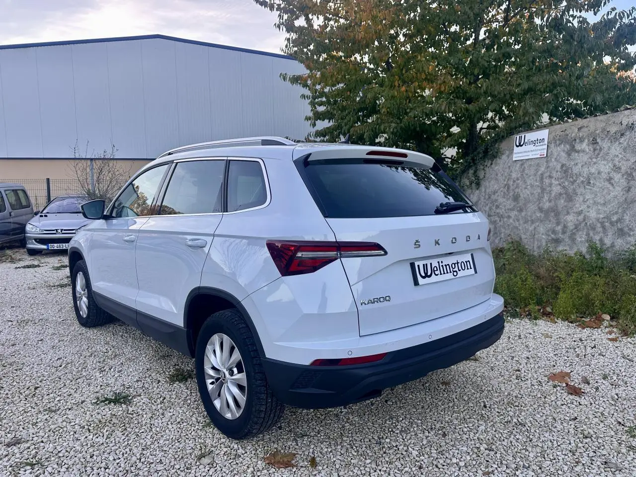Vue 3/4 arrière droite d'un SUV SKODA KAROQ blanc 2024 avec vitres teintées et barres de toit.