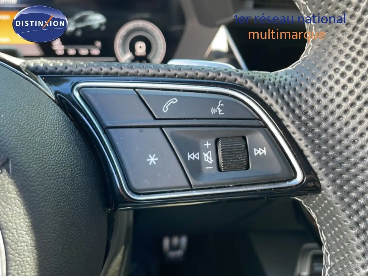 Gros plan sur les commandes du volant en cuir perforé de l'Audi A3 Sportback bleu Navarre, version hybride rechargeable 2025.