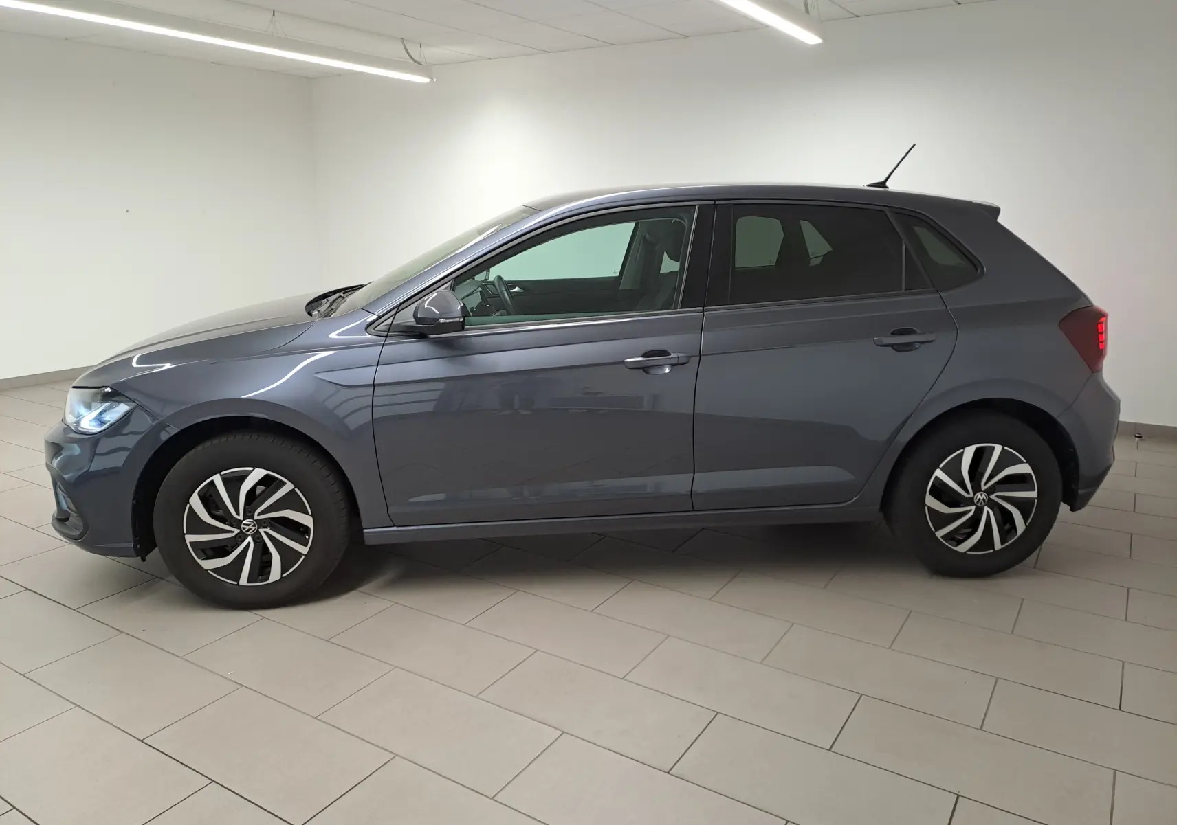 Volkswagen Polo gris cendre vue de profil côté gauche dans un intérieur lumineux avec jantes distinctives.