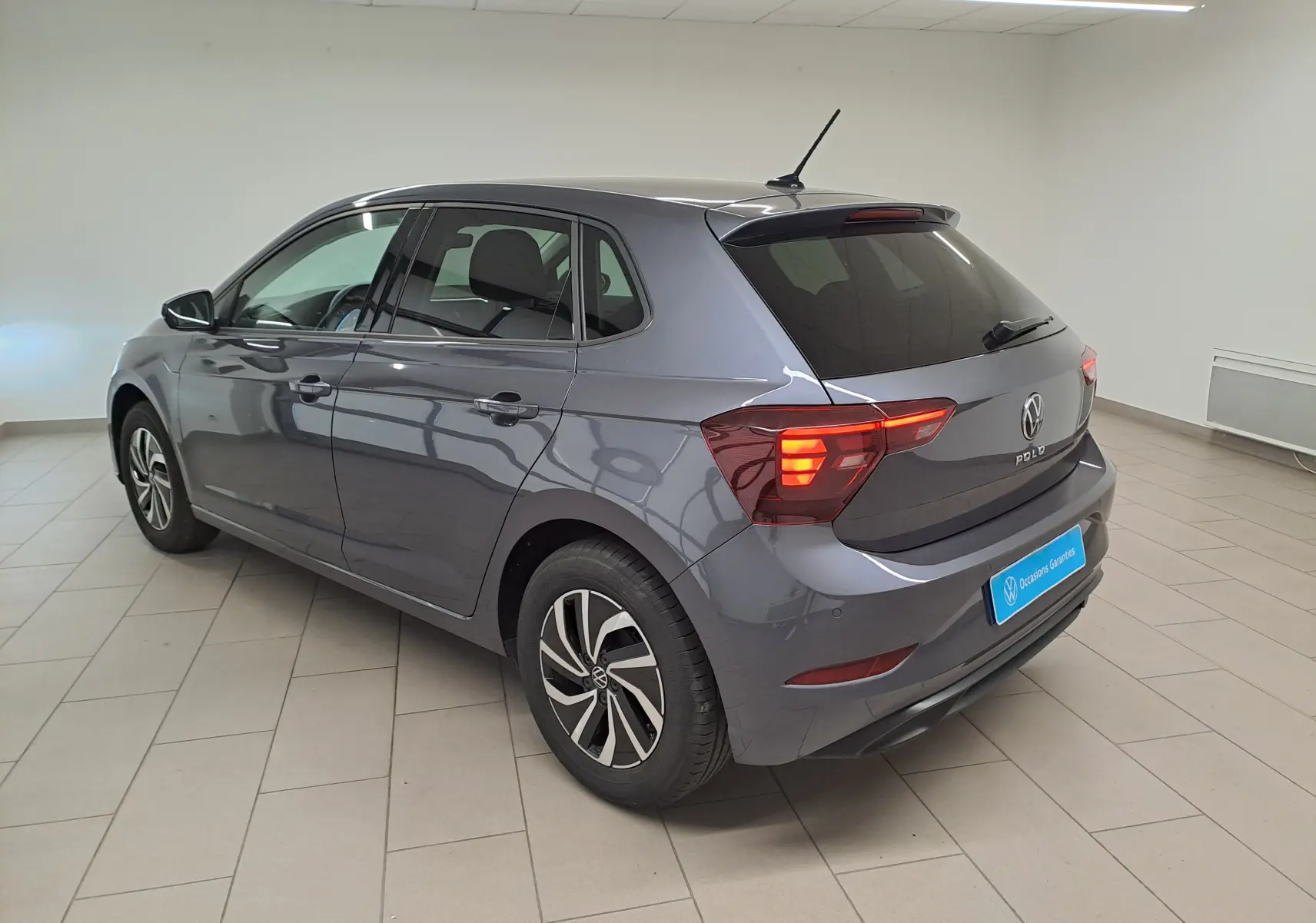Volkswagen Polo gris cendre vue 3/4 arrière droit en intérieur, feux arrière allumés et jantes spécifiques VW Edition.