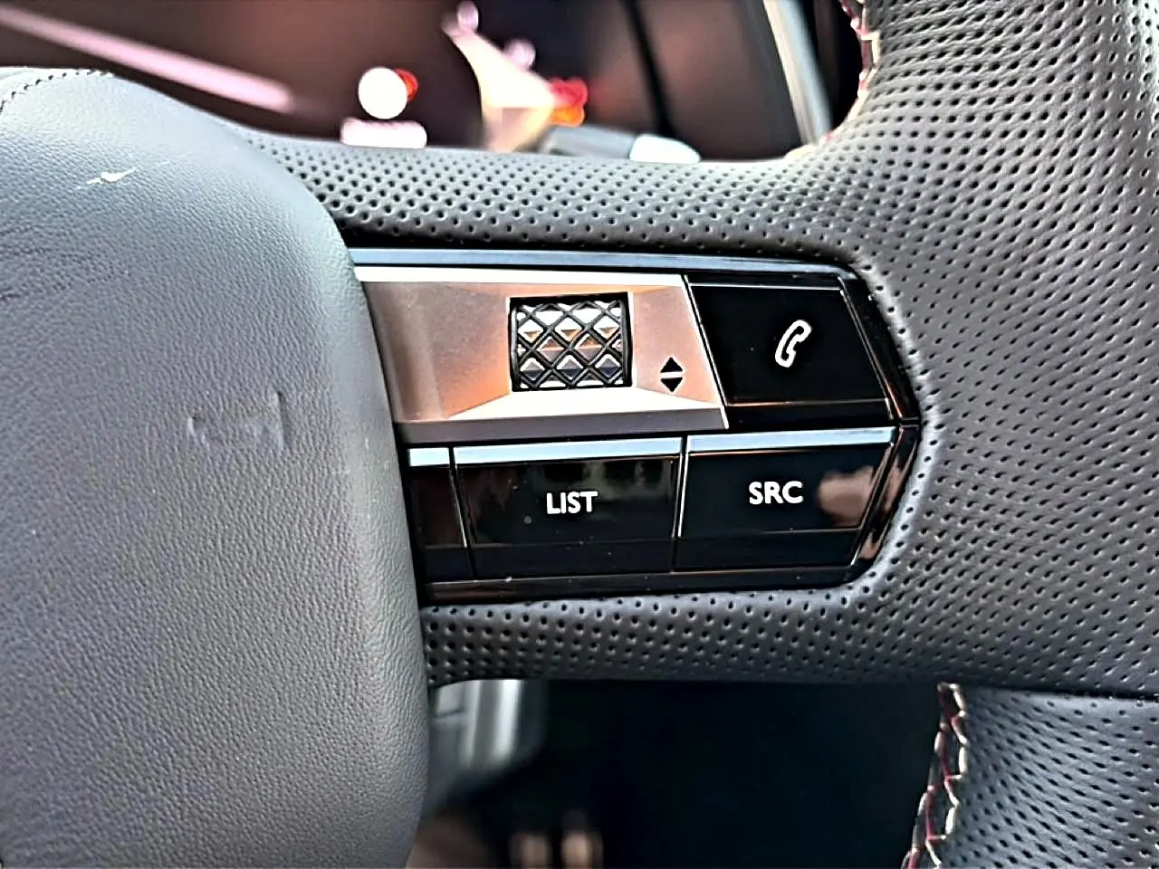 Gros plan sur les commandes noires et argentées au volant en cuir perforé du DS7 1.5 BlueHDi 130 Performance Line noir.