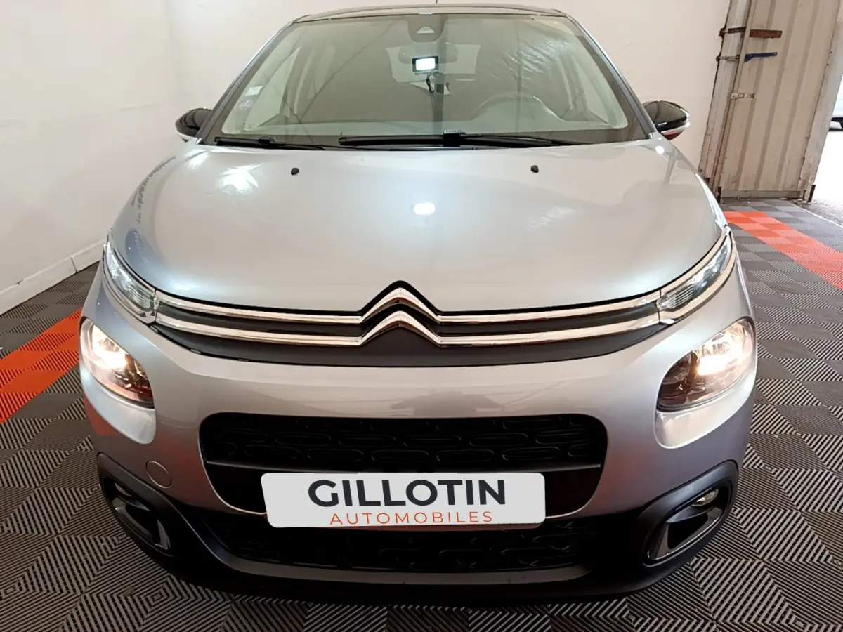 Vue frontale d'une Citroën C3 gris clair 2019 avec phares allumés et calandre distinctive en double chevron.