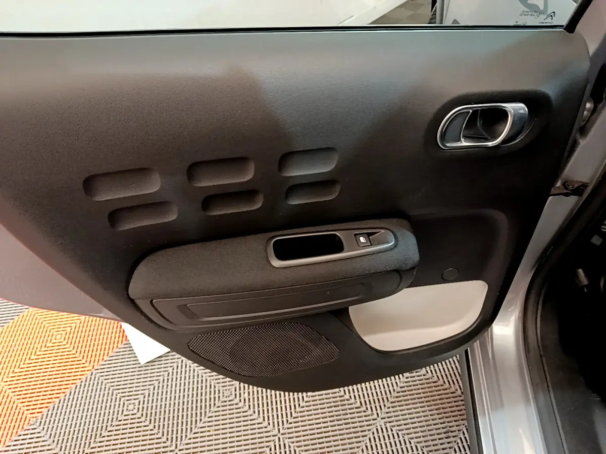Gros plan sur la porte intérieure côté droit gris clair de la Citroën C3 avec poignée chromée et commande de fenêtre.