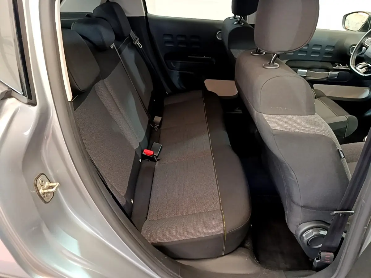 Vue intérieure côté arrière droit de la Citroën C3 gris clair, montrant la banquette arrière et les sièges avant en tissu noir.