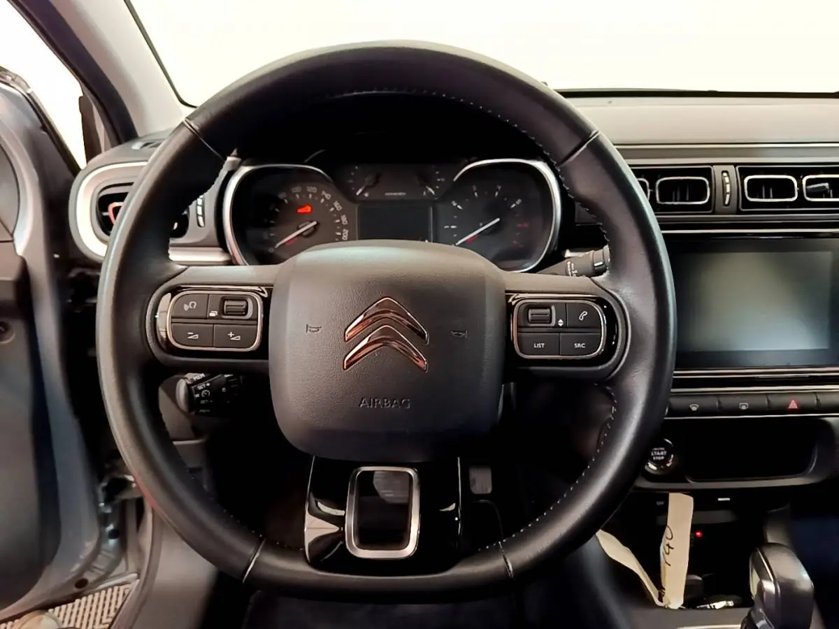 Vue intérieure centrée sur le volant cuir de la Citroën C3 gris clair avec tableau de bord et écran tactile.