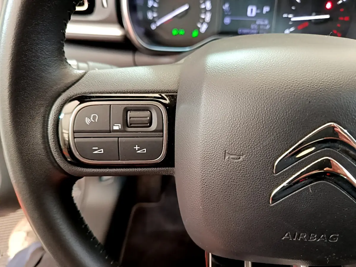 Gros plan sur le volant cuir noir de la Citroën C3 gris clair, avec commandes vocales et volume intégrées à gauche.