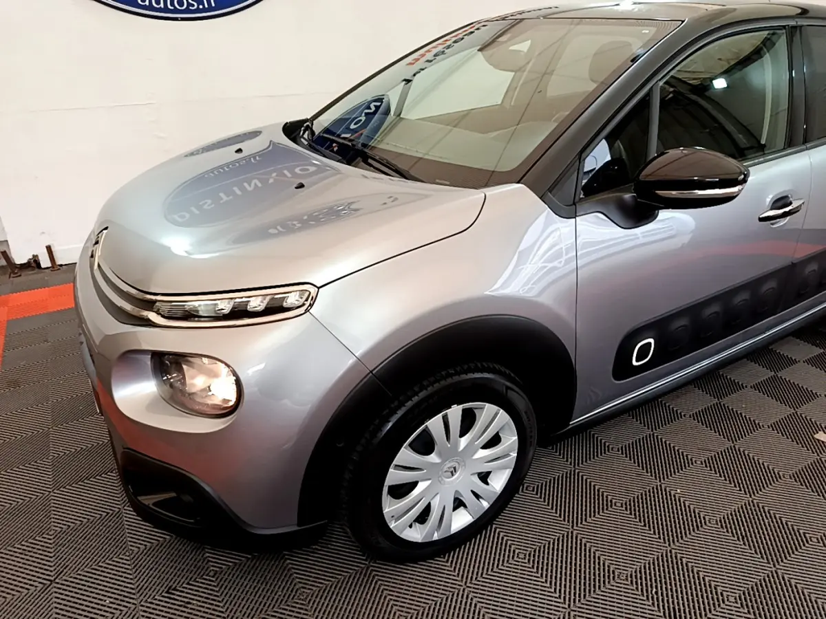 Vue 3/4 avant droit d'une Citroën C3 gris clair avec protections latérales noires et jantes argentées.