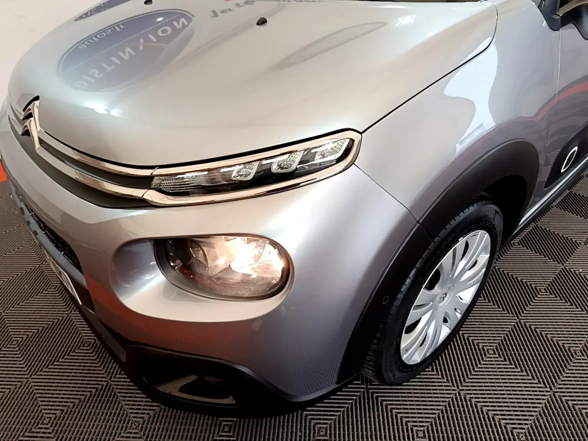Vue 3/4 avant droit d'une Citroën C3 gris clair avec phares allumés et jantes acier au design spécifique.