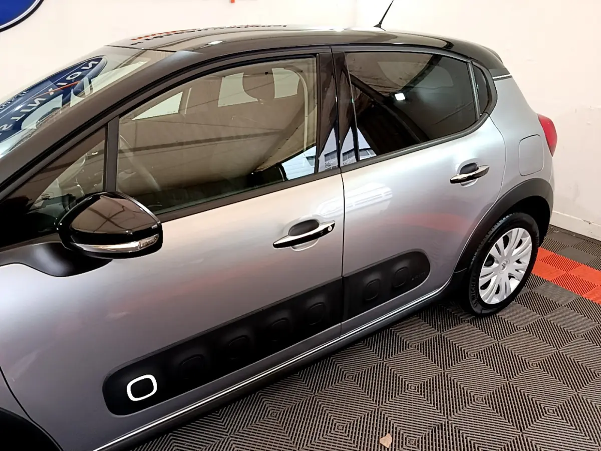 Profil côté gauche d'une Citroën C3 gris clair avec protections noires caractéristiques et rétroviseur noir brillant.