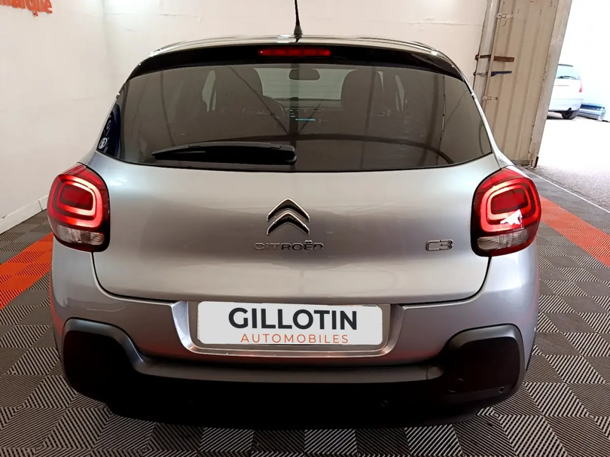 Vue arrière d'une Citroën C3 gris clair avec feux arrière allumés dans un garage fermé.