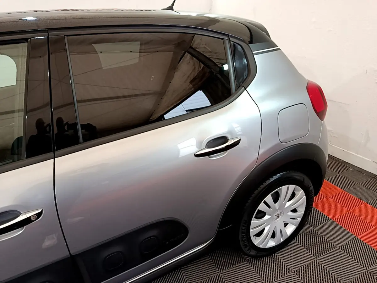 Vue latérale arrière droite d'une Citroën C3 gris clair avec poignées chromées et protections noires sur porte.