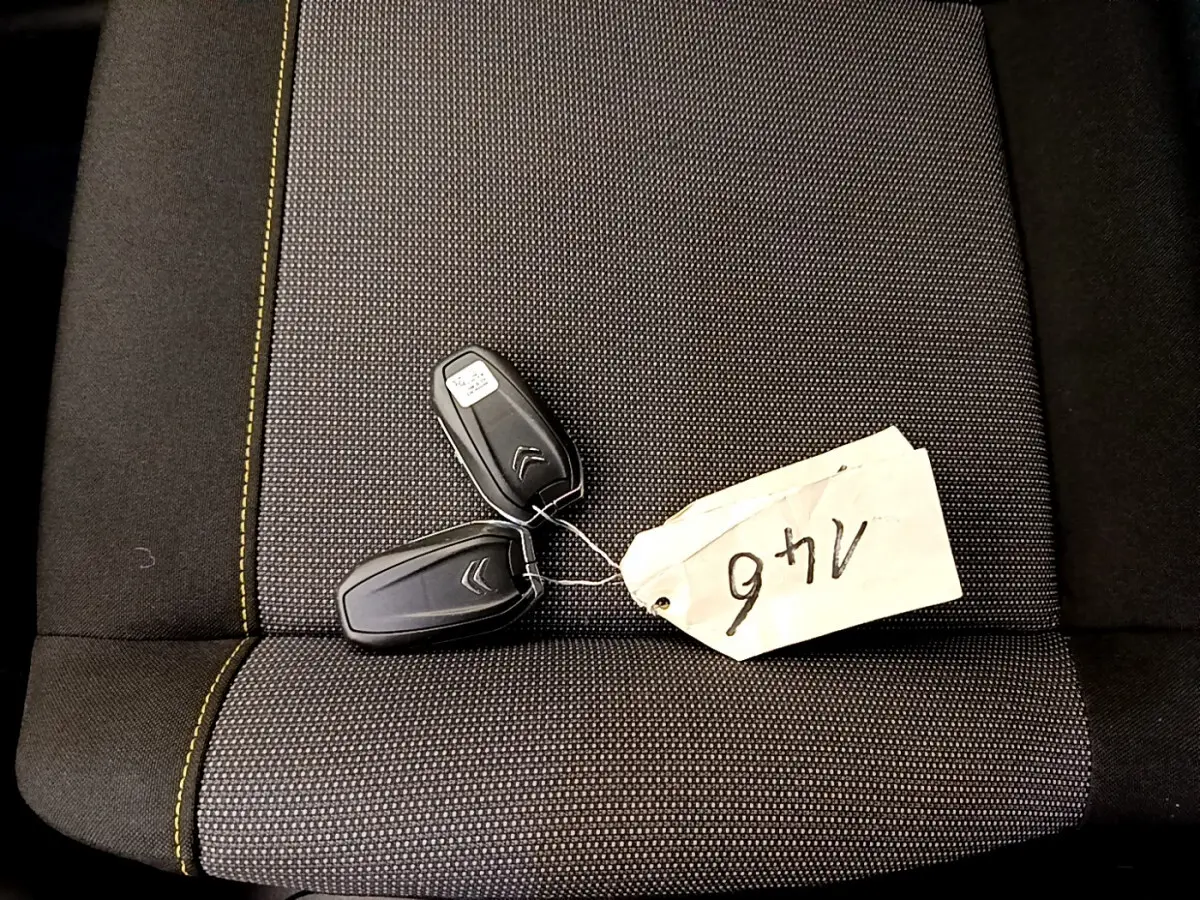 Clé de voiture Citroën posée sur un siège tissu gris foncé avec surpiqûres jaunes, vue de dessus.